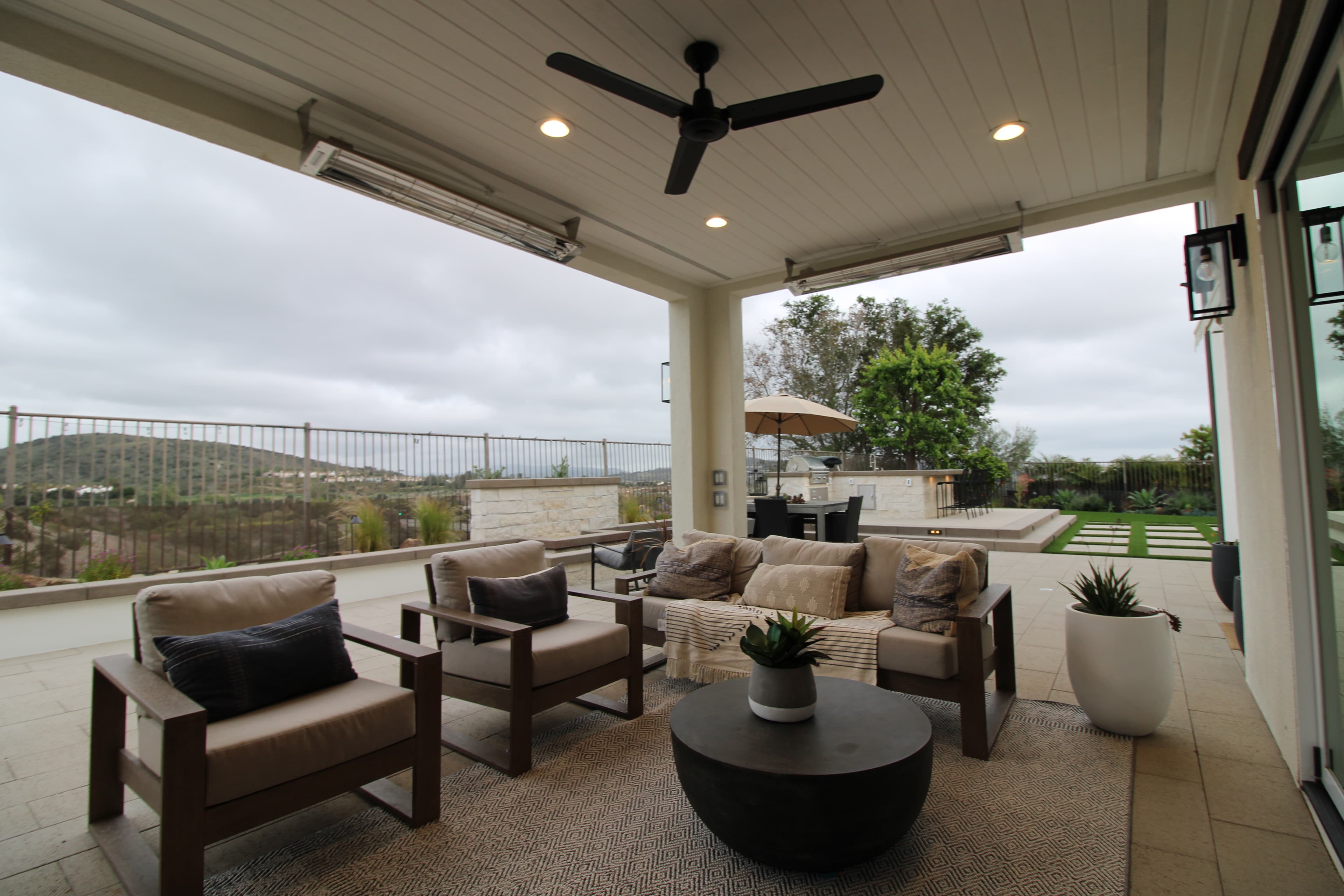 Modern covered patio with neutral furniture, a ceiling fan, and scenic views of rolling hills.